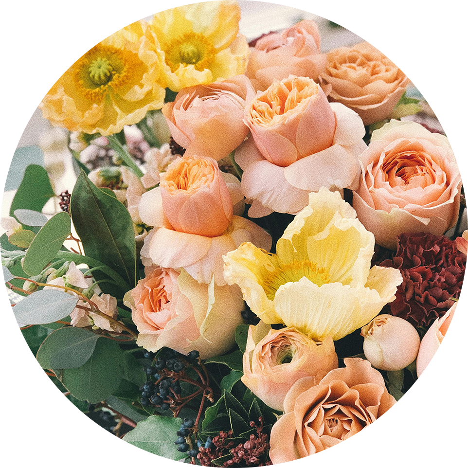 A bouquet of soft peach roses, pale pink buds, and bright yellow poppies rests among fresh greenery, creating a warm and uplifting display that reflects both beauty and comfort.